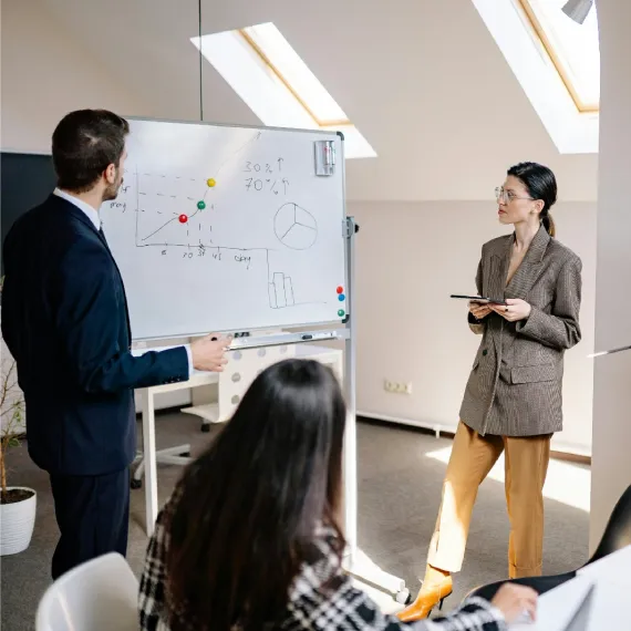 A trainer walks a small class through charts on a whiteboard